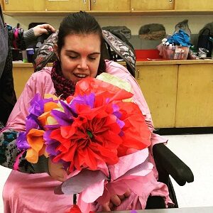 A woman in a wheelchair wearing a pink shirt s holding a bouquet of flowers.
