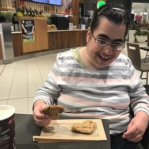 A woman is sitting at a table in a food court with a heart-shaped cookie in front of her. 