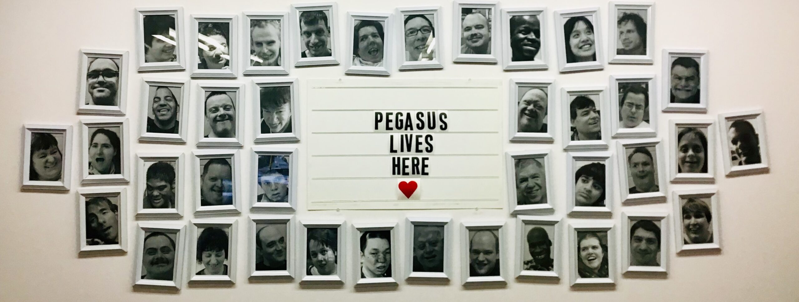 Image depicting a white wall with black and white pictures surrounding the words "Pegasus Lives Here"