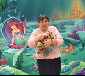 A woman wearing a pink shirt is holding drums in the background is an image of Ariel from The Little Mermaid.