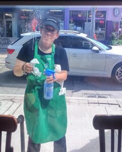 A woman wearing a green Starbucks apron is cleaning a window.