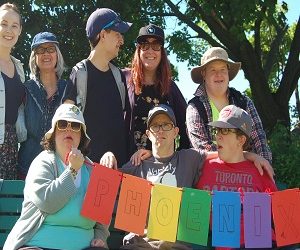 A group of Pegasus participants and staff holding a multi-coloured banner that says "Phoenix". The group is outside at the annual picnic.
